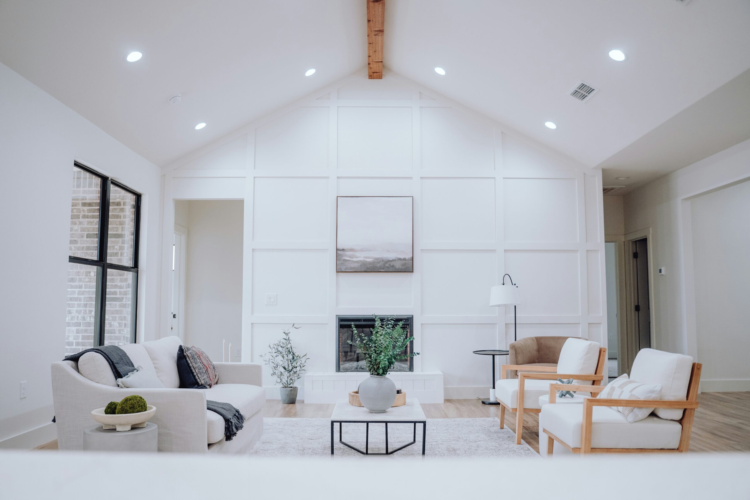 Bright modern living room with vaulted ceilings, white paneled walls, minimalist furniture, and a central fireplace.
