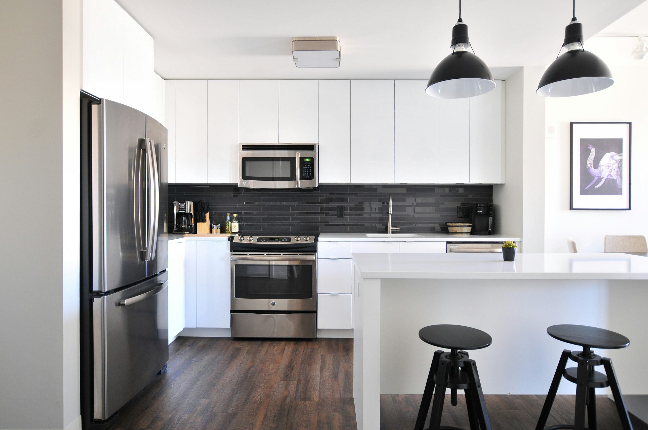 Modern kitchen with sleek white cabinets, black subway tile backsplash, stainless steel appliances, and a white island with black stools.