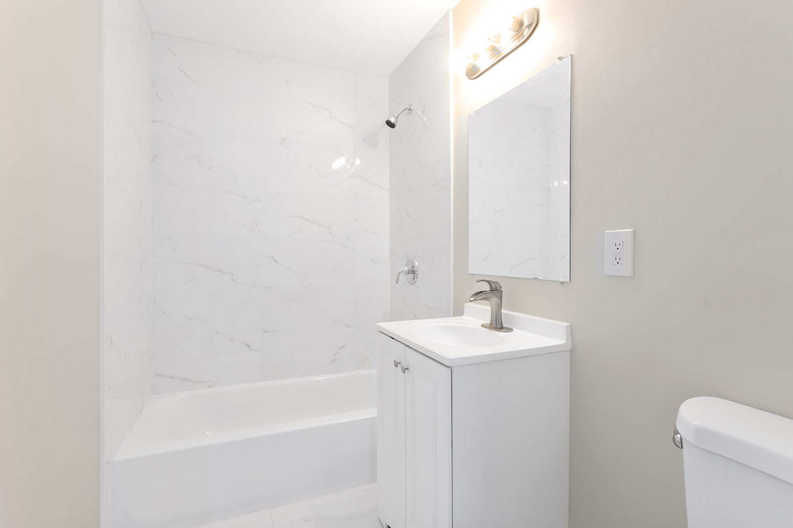 Modern bathroom with a white vanity, chrome faucet, marble-style tile shower, and soft beige walls.