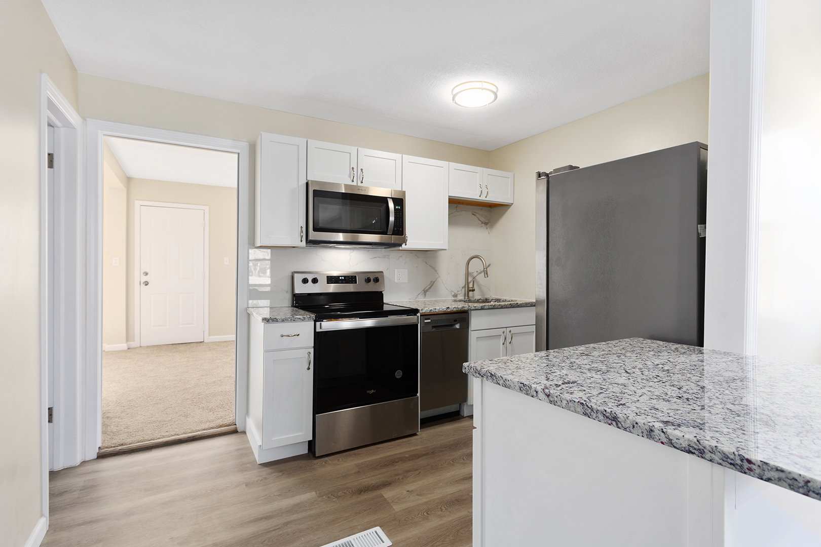 Compact modern kitchen with white cabinets, granite countertops, stainless steel appliances, and a marble backsplash.