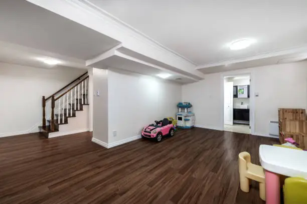 Spacious basement with dark wood flooring, white walls, a play area with toys, and a staircase leading to the upper level.