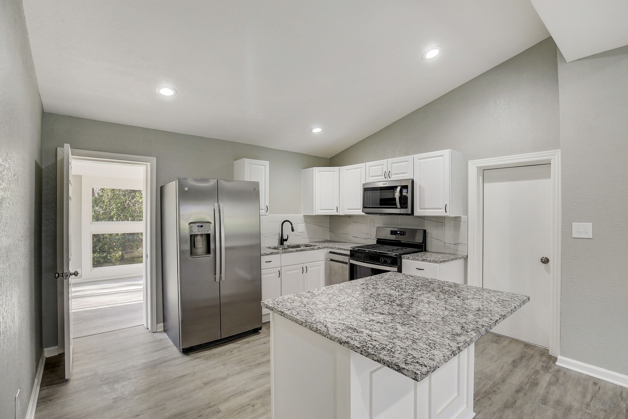 Modern kitchen with white cabinets, granite countertops, stainless steel appliances, and light wood flooring.