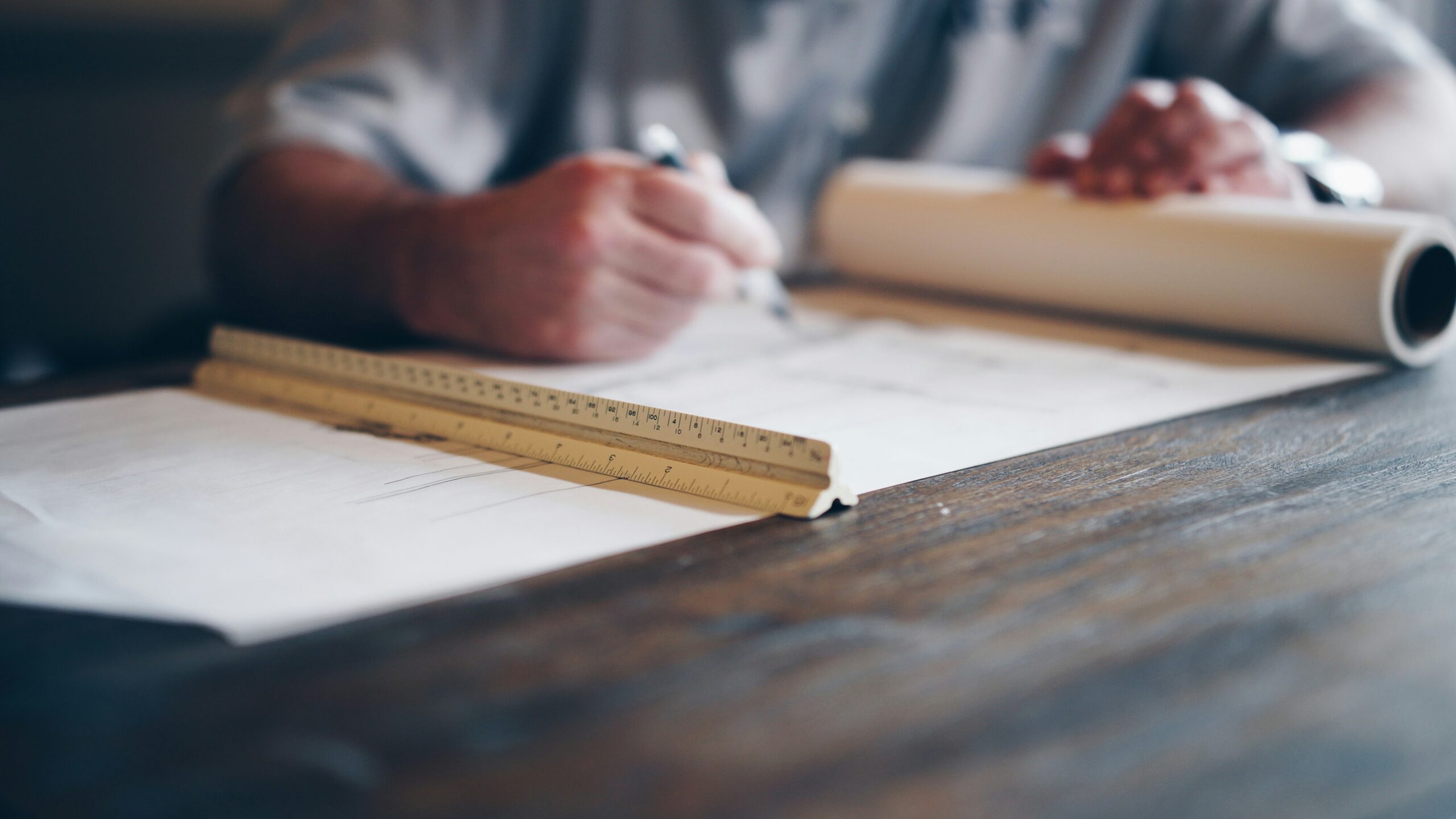Architect or designer working on blueprints with a ruler on a wooden desk.